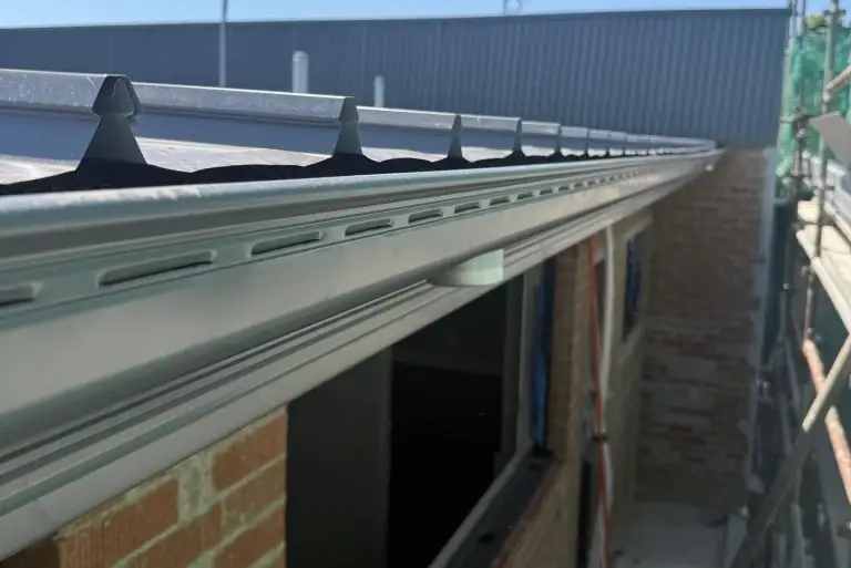 Grey gutter showing overflow slots and white downpipe elbow attached to corrugated roof edge