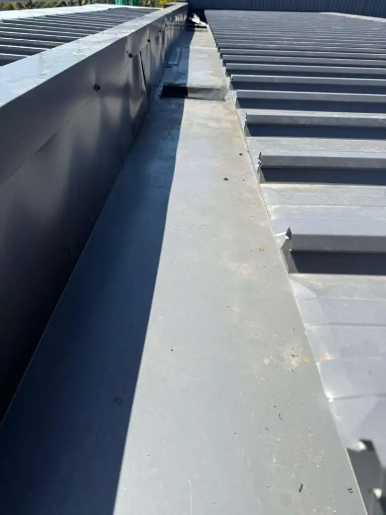 Installation detail of roof gutter on parapet edge, grey metal box gutter with flashing and ribbed corrugated roof