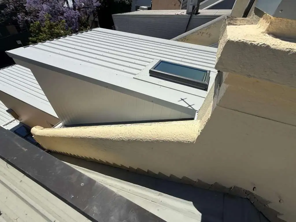 Top-down view of light grey metal roof on dormer, ribbed corrugated panels with skylight and surrounding rooftop setting